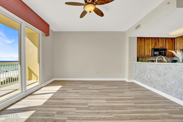 unfurnished living room with a water view, ceiling fan, and light hardwood / wood-style flooring