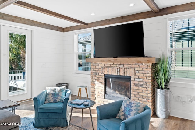 living room with beamed ceiling, hardwood / wood-style floors, a brick fireplace, and wood walls