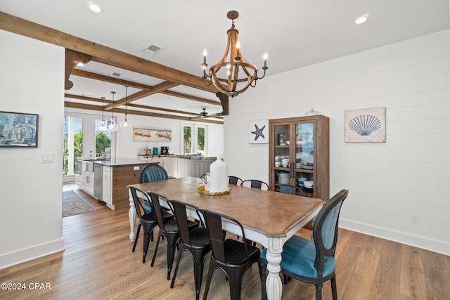 dining space with ceiling fan with notable chandelier, beam ceiling, light wood-type flooring, and french doors