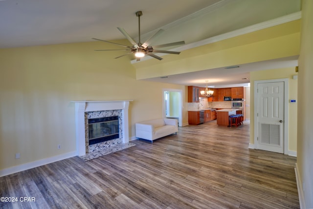 unfurnished living room with vaulted ceiling, a tile fireplace, dark wood-type flooring, ceiling fan with notable chandelier, and crown molding