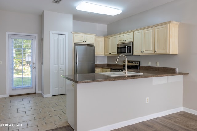 kitchen with appliances with stainless steel finishes, kitchen peninsula, light wood-type flooring, and cream cabinetry