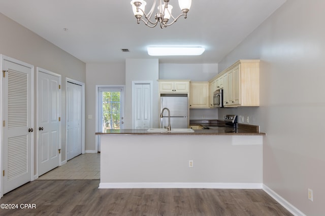 kitchen with appliances with stainless steel finishes, cream cabinetry, kitchen peninsula, light hardwood / wood-style floors, and decorative light fixtures