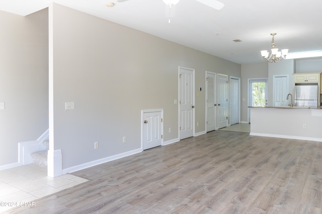 unfurnished living room with sink, ceiling fan with notable chandelier, and light wood-type flooring