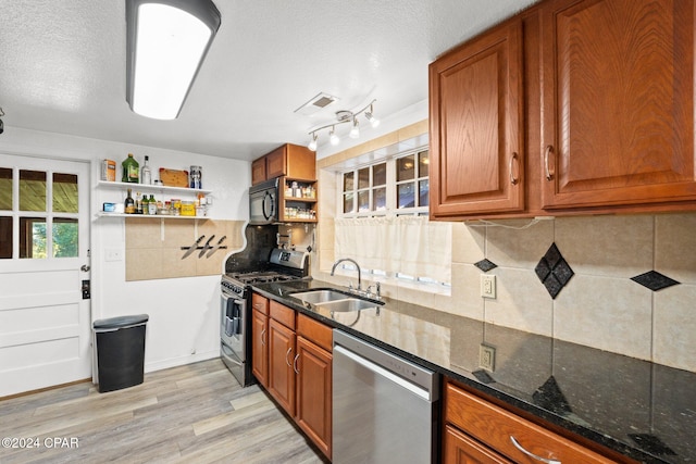 kitchen with stainless steel appliances, light hardwood / wood-style floors, sink, dark stone countertops, and backsplash