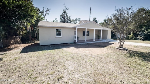 view of front of house featuring covered porch, stucco siding, fence, and a front lawn