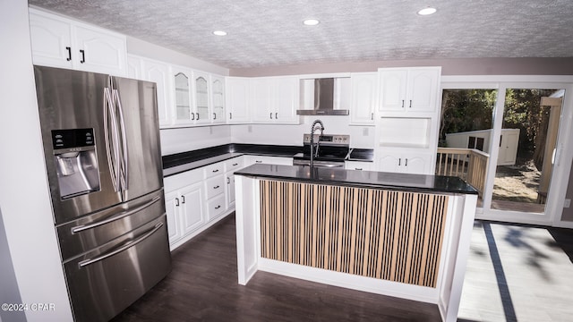 kitchen featuring stainless steel appliances, wall chimney exhaust hood, white cabinets, dark wood-type flooring, and a center island with sink