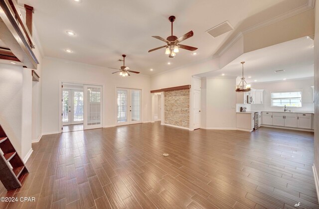 unfurnished living room with sink, ceiling fan with notable chandelier, french doors, dark hardwood / wood-style flooring, and ornamental molding