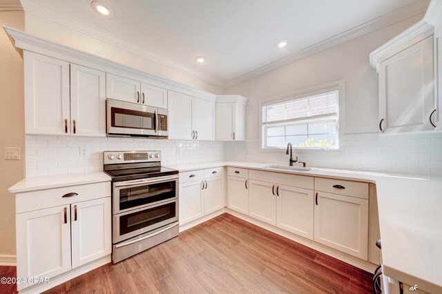 kitchen with white cabinets, light wood-type flooring, ornamental molding, sink, and stainless steel appliances