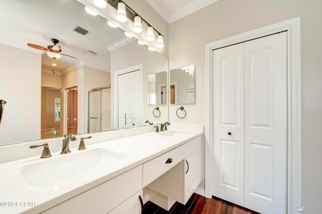 bathroom with wood-type flooring, a shower with shower door, ceiling fan, vanity, and ornamental molding