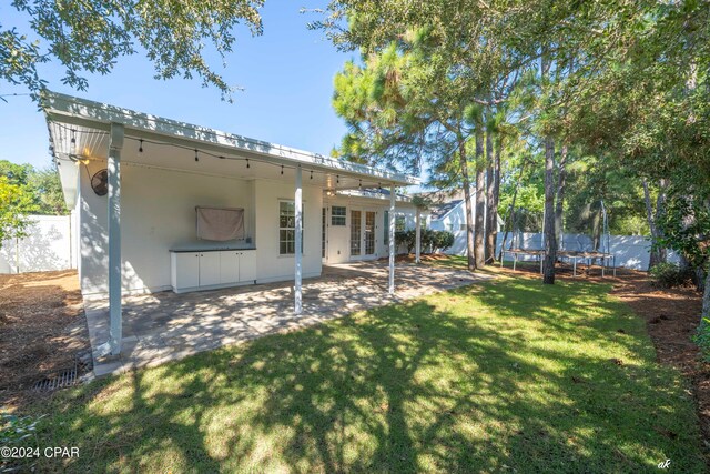 back of property with a trampoline, a patio, and a lawn