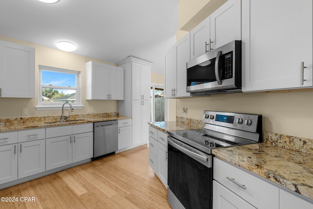 kitchen featuring stainless steel appliances, sink, light stone countertops, white cabinetry, and light hardwood / wood-style floors