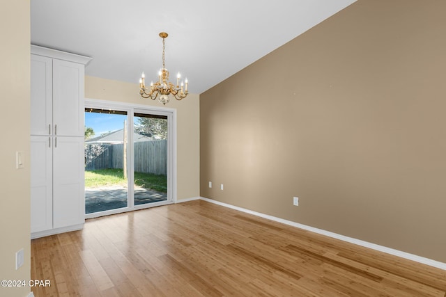 spare room featuring a notable chandelier, wood-type flooring, and lofted ceiling