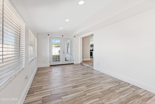 empty room featuring french doors, light hardwood / wood-style floors, and vaulted ceiling