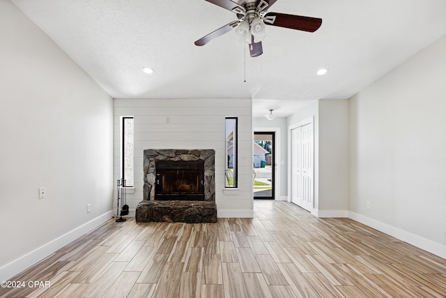 unfurnished living room featuring a stone fireplace, light hardwood / wood-style flooring, a textured ceiling, and ceiling fan