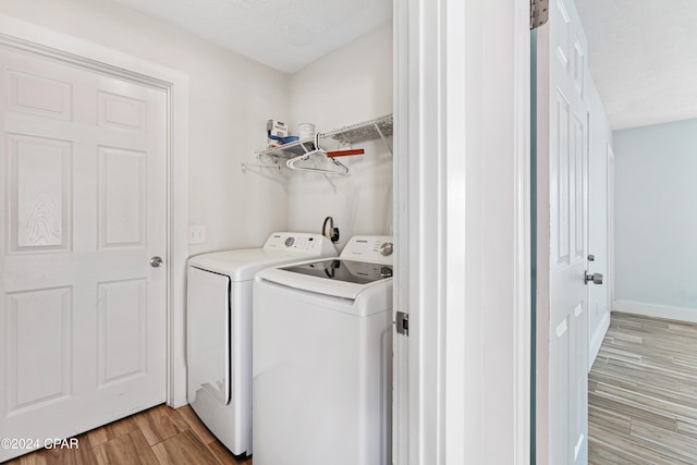 laundry area with a textured ceiling, light hardwood / wood-style flooring, and washer and clothes dryer