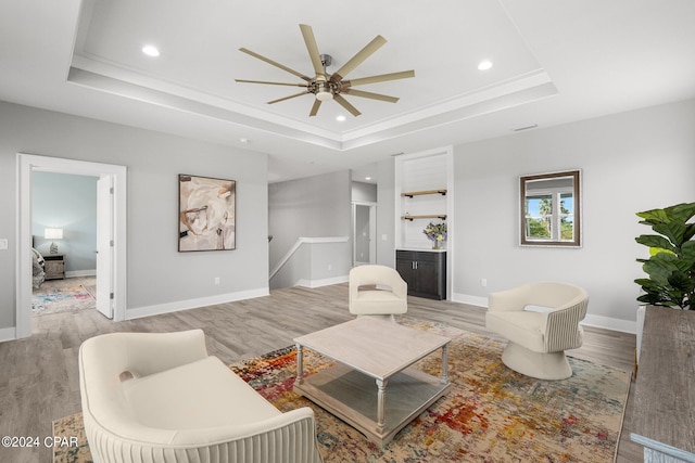 living room with light hardwood / wood-style floors, a tray ceiling, and ceiling fan