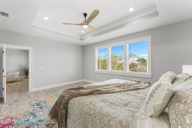 bedroom with ornamental molding, light hardwood / wood-style flooring, a tray ceiling, and ceiling fan