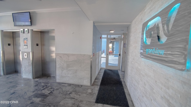 hall with a wainscoted wall, ornamental molding, tile walls, and elevator