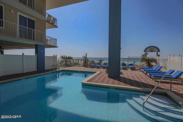 pool with a water view, fence, and a patio