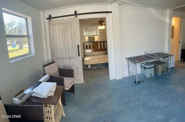 living area with a barn door, concrete flooring, and ceiling fan