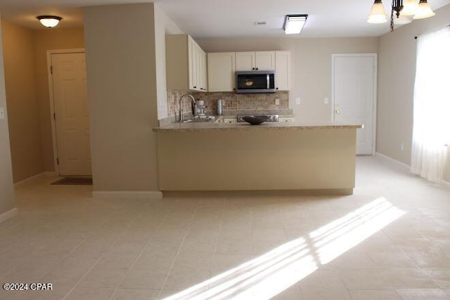 kitchen featuring decorative backsplash, kitchen peninsula, sink, light tile patterned floors, and white cabinetry