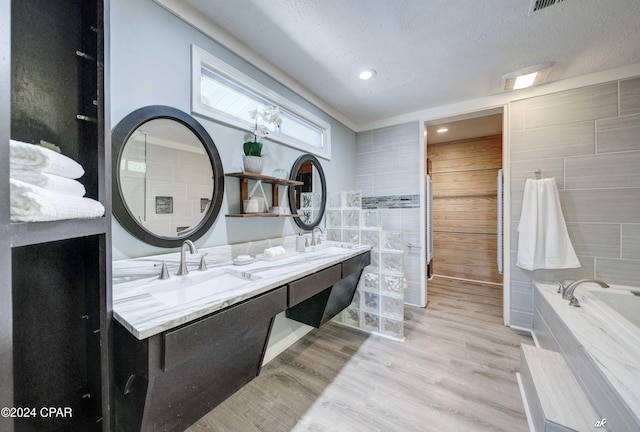 bathroom with a tub to relax in, hardwood / wood-style floors, a textured ceiling, vanity, and tile walls