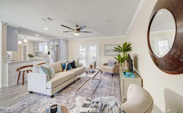 living room with french doors, a textured ceiling, ceiling fan, crown molding, and light hardwood / wood-style flooring