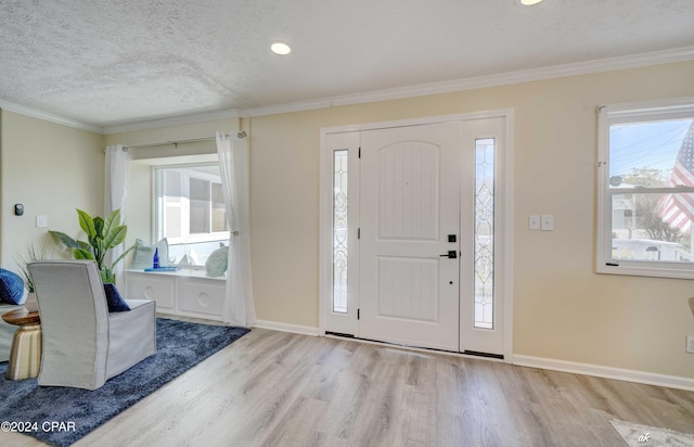 foyer entrance featuring a textured ceiling, light wood-type flooring, and crown molding