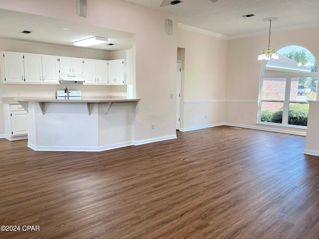 kitchen with dark wood-type flooring, a breakfast bar area, white cabinetry, an inviting chandelier, and ornamental molding