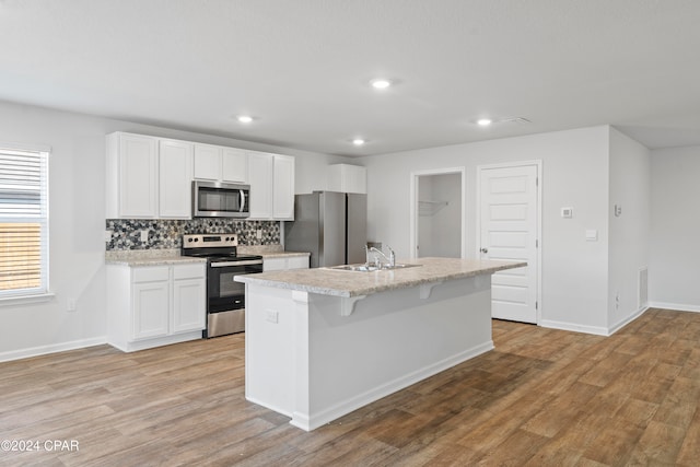 kitchen featuring an island with sink, stainless steel appliances, white cabinetry, and light hardwood / wood-style floors