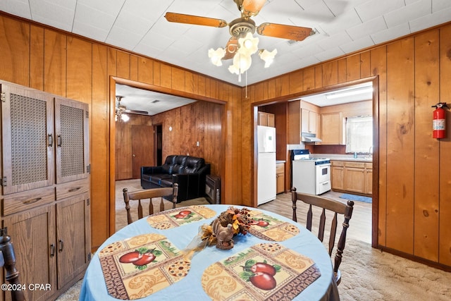 dining area with sink, wooden walls, light colored carpet, and ceiling fan