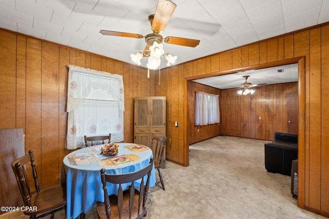 dining area with ceiling fan, light colored carpet, and wood walls