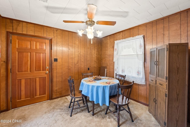 dining area featuring ceiling fan, light carpet, and wood walls