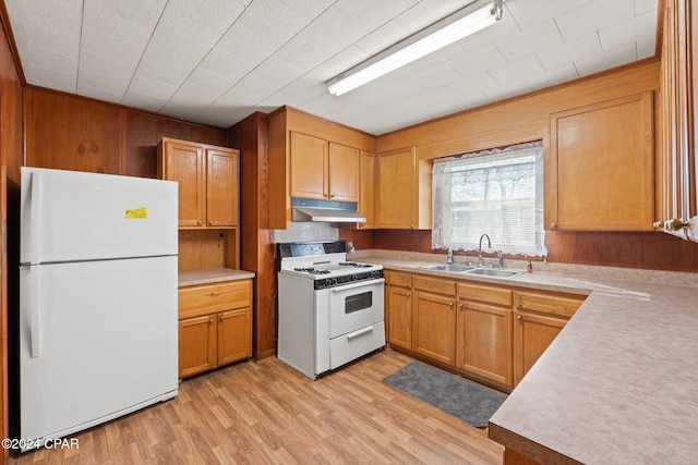 kitchen featuring white appliances, light hardwood / wood-style floors, sink, and wooden walls