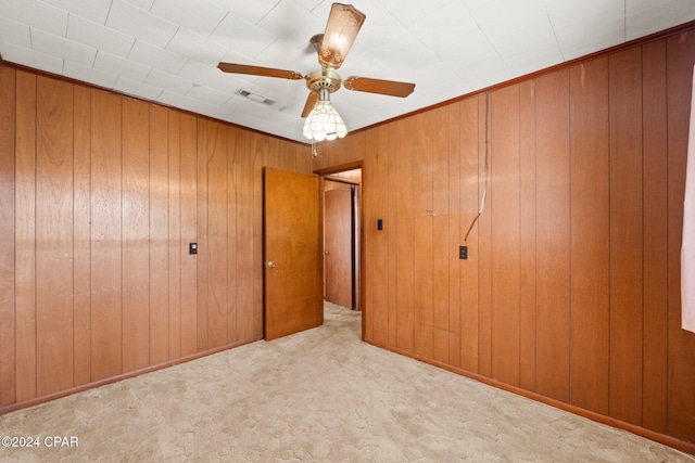 unfurnished bedroom featuring wood walls, light colored carpet, and ceiling fan