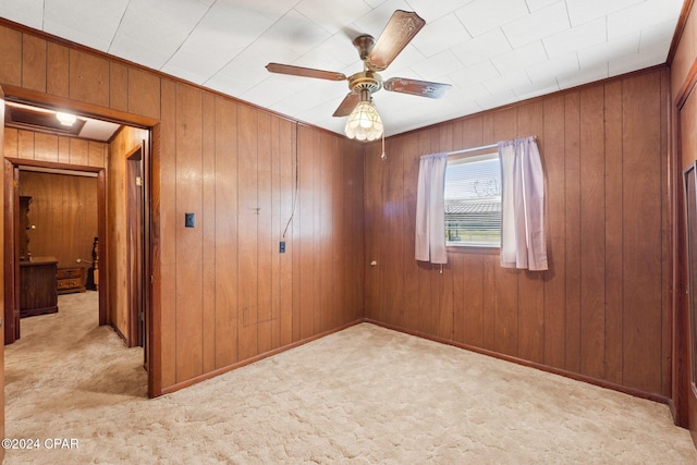 carpeted spare room featuring ceiling fan and wood walls