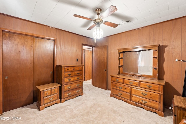 bedroom with light carpet, a closet, wooden walls, and ceiling fan