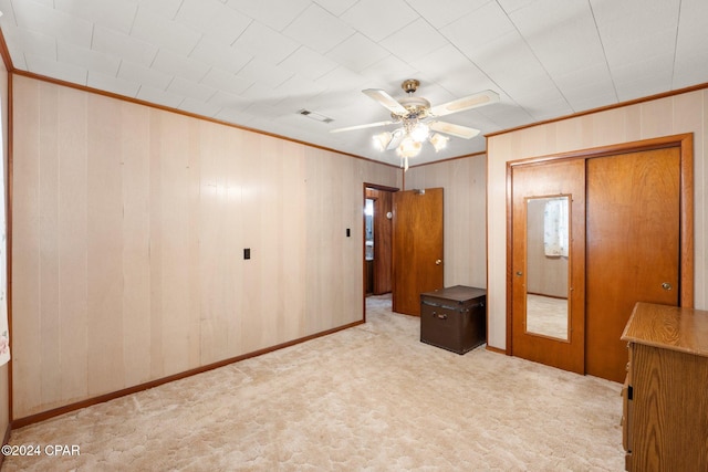 unfurnished bedroom with a closet, wood walls, light colored carpet, and ceiling fan