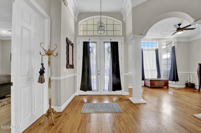 foyer entrance featuring a textured ceiling, wood-type flooring, ceiling fan with notable chandelier, and decorative columns