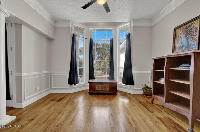 interior space featuring ornate columns, light hardwood / wood-style floors, crown molding, and a textured ceiling