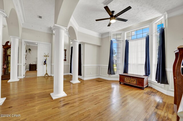 interior space featuring a textured ceiling, ornate columns, ceiling fan, ornamental molding, and light hardwood / wood-style flooring