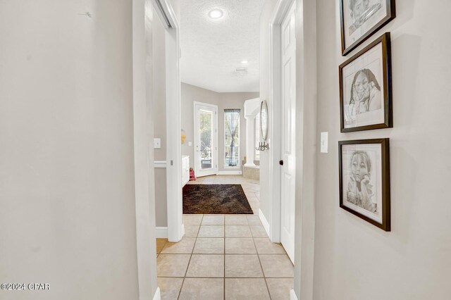 hallway with a textured ceiling and light tile patterned floors