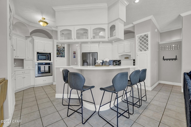 kitchen with white cabinets, a kitchen island, appliances with stainless steel finishes, a breakfast bar, and ornamental molding