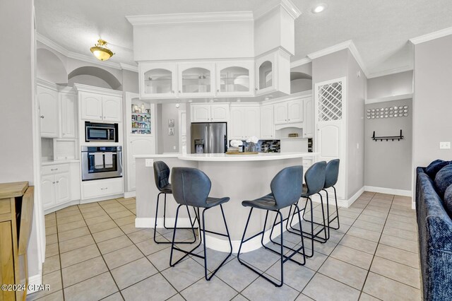 kitchen featuring ornamental molding, a breakfast bar, white cabinets, and stainless steel appliances