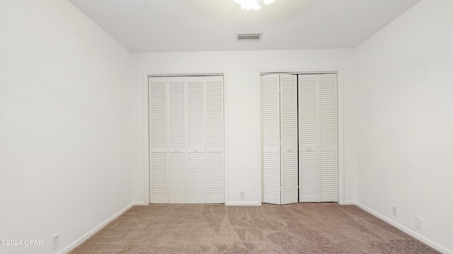 unfurnished bedroom featuring baseboards, visible vents, multiple closets, and carpet floors