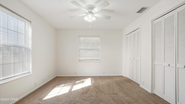 unfurnished bedroom featuring visible vents, multiple closets, carpet, and baseboards