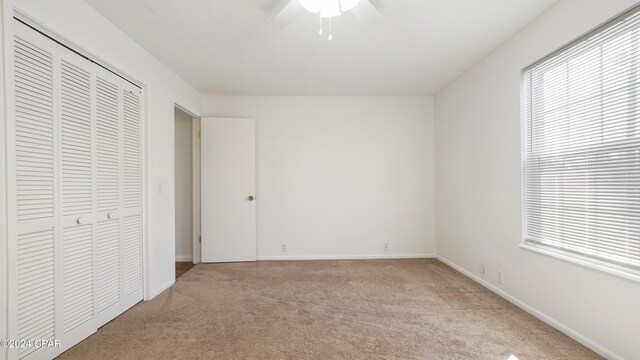 unfurnished bedroom featuring a closet, multiple windows, light colored carpet, and baseboards