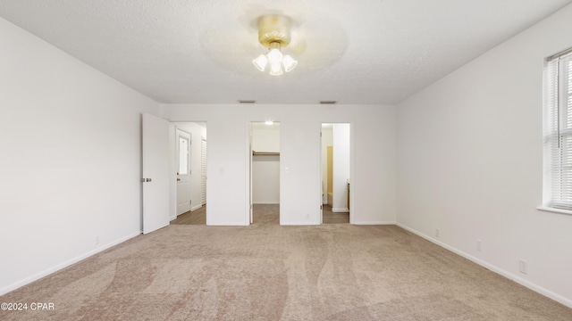 unfurnished bedroom featuring a spacious closet, light colored carpet, baseboards, and a textured ceiling