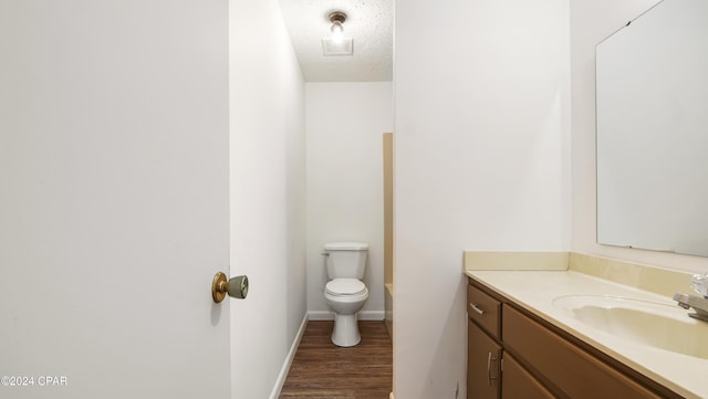 bathroom with vanity, wood finished floors, baseboards, a textured ceiling, and toilet