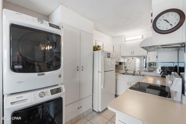 kitchen with light tile patterned floors, stacked washer and dryer, white cabinetry, light countertops, and freestanding refrigerator